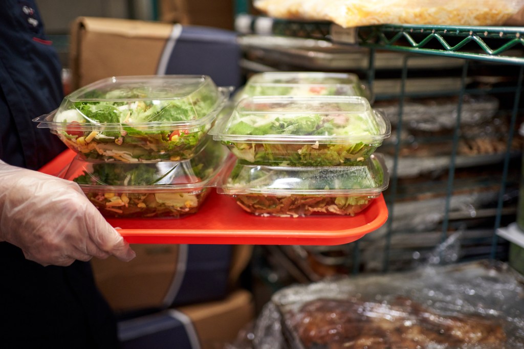 A team member carrying salads on a red tray.