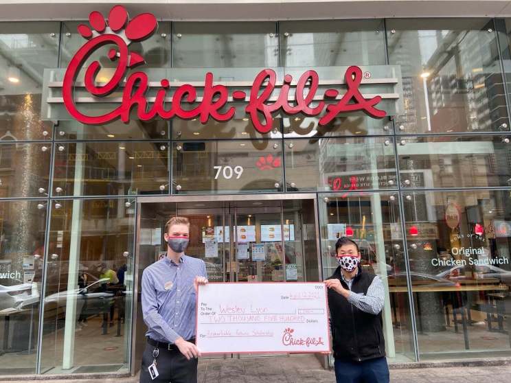 Two men holding a large check in front of a Chick-fil-A restaurant entrance.