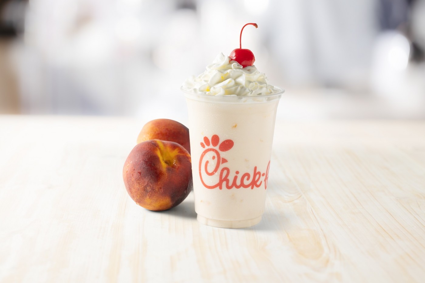 One cup with a peach shake, accompanied by two peaches on a wooden surface.