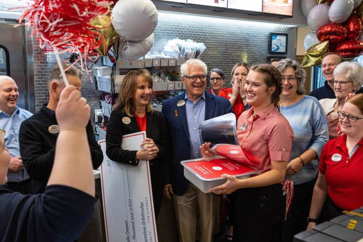A group of people celebrating indoors with balloons and a large ceremonial check.