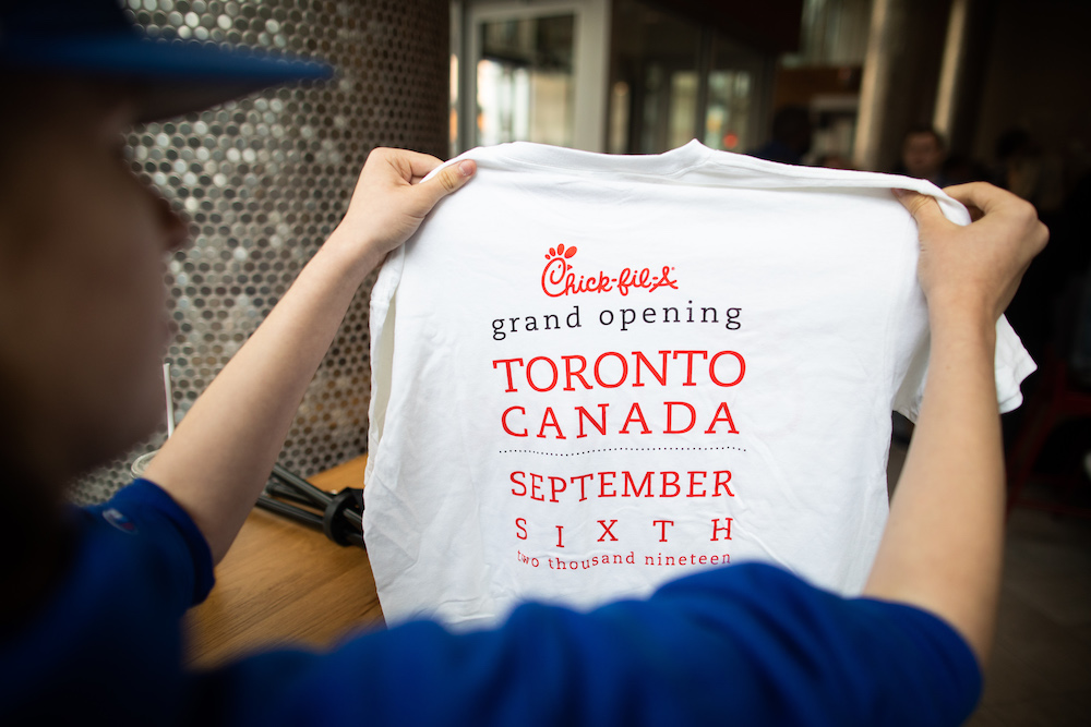 Person holding a white Chick-fil-A t-shirt promoting the grand opening in Toronto, Canada on September 6, 2019.