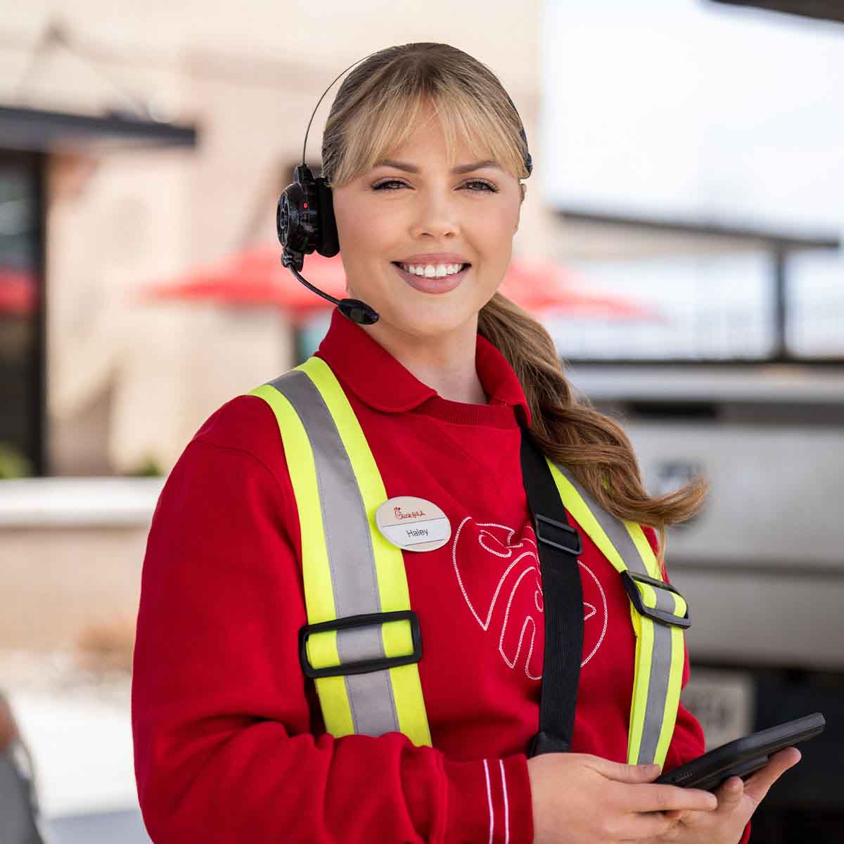 A Team Member wearing a safety vest and headset standing outside a Chick-fil-A Restaurant
