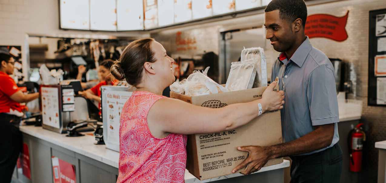 Chick-fil-A team members hands a box of food donations to a community member.