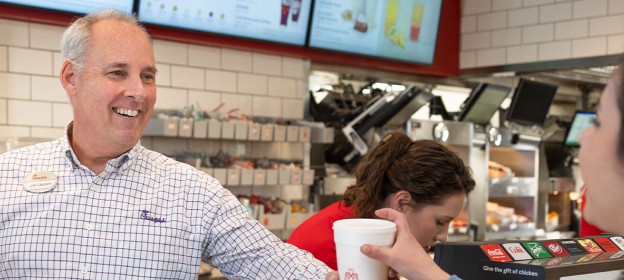 A Chick-fil-A Restaurant Director smiling and giving a customer a beverage