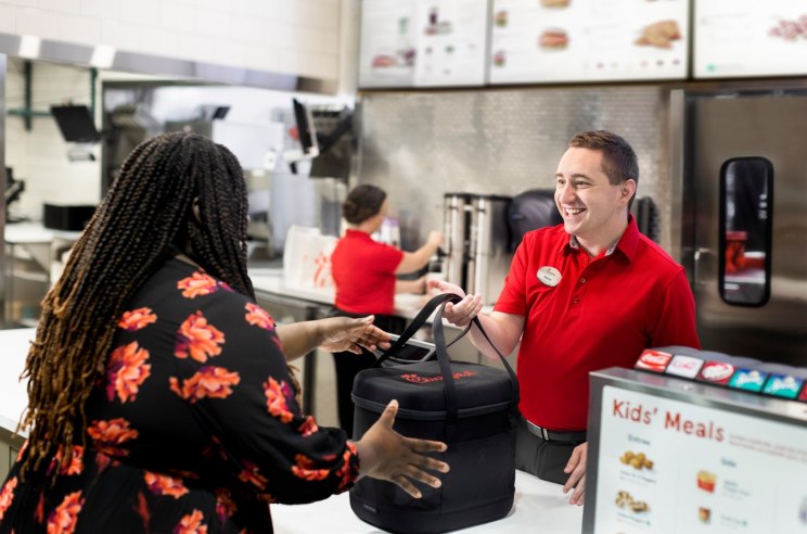 Smiling Chick-fil-A team member handing an insulated bag to a customer.