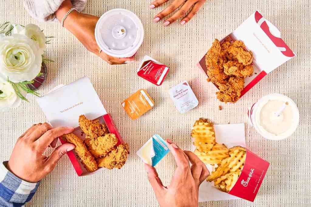 Top-down view of a meal with chicken strips, waffle fries, sauce packets, a drink, and a flower bouquet.