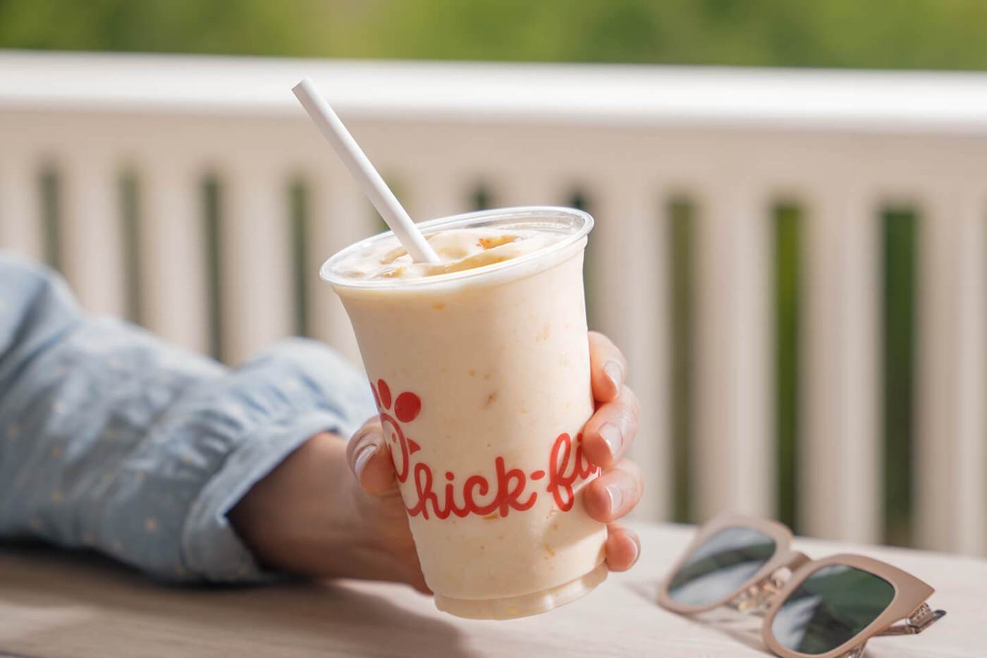 Hand holding a Chick-fil-A Peach Milkshake with sunglasses on the table.