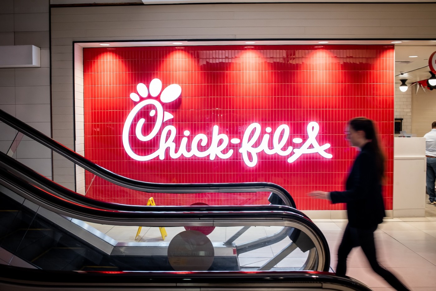 Chick-fil-A logo on a red wall behind escalators.
