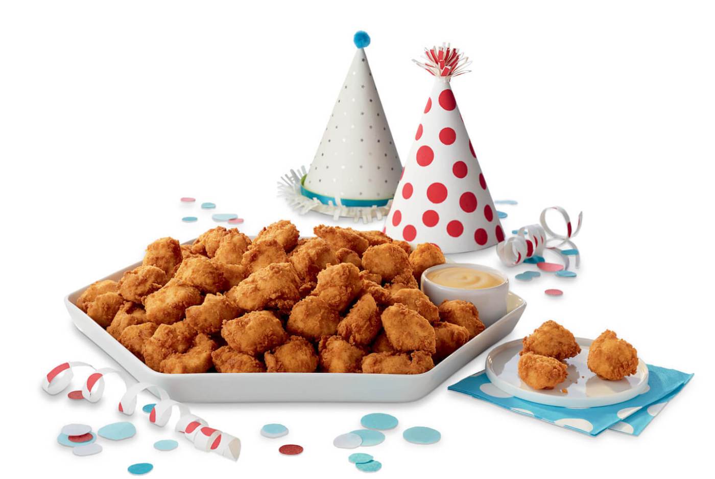 Party platter of fried chicken nuggets with dipping sauce, party hats, and confetti.