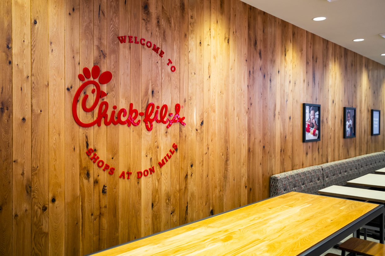 Interior of a Chick-fil-A with a wooden wall featuring the restaurant's logo and text "WELCOME TO Chick-fil-A SHOPS AT DON MILLS"