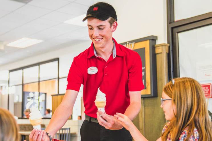 A team member delivers ice cream cones to two customers in a Chick-fil-A restaurant.
