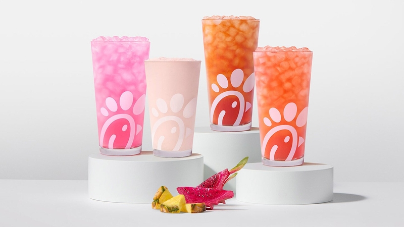 A glass of a Pineapple Dragonfruit Lemonade, Frosted Lemonade, Iced Tea and Sunjoy on risers with pieces of pineapple and dragonfruit next to them.