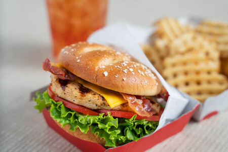 Close-up of a Chick-fil-A grilled chicken Sandwich, held by two hands, with waffle fries and a drink in the background.