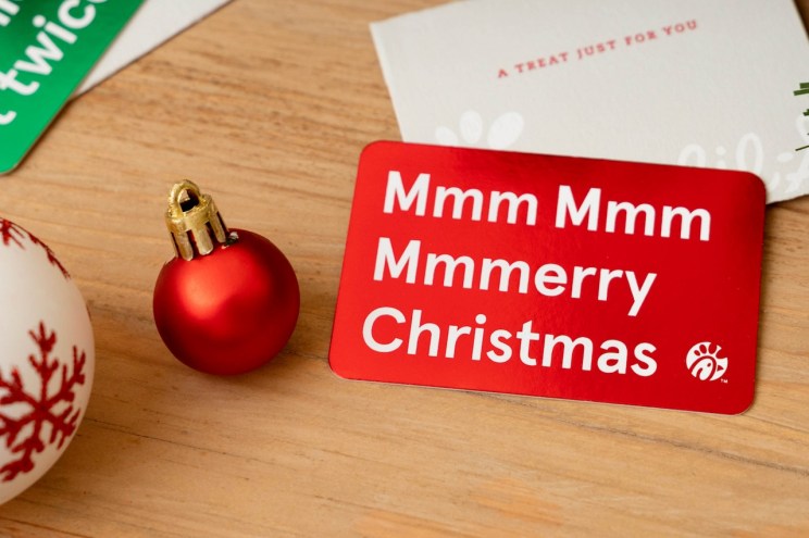 Red Chick-fil-A gift card reading “Mmm Mmm Mmmerry Christmas” with Christmas ornaments on a wooden surface.