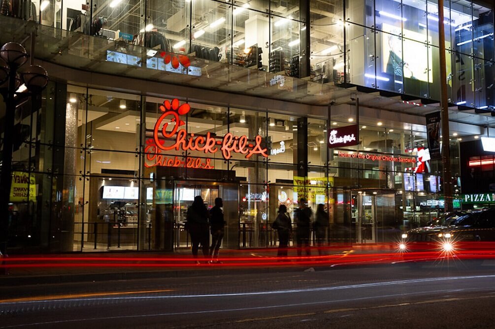 Nighttime street view of a Chick-fil-A restaurant with a glass facade and red logo.