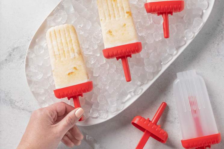 Creamy peach popsicles with red handles on ice.