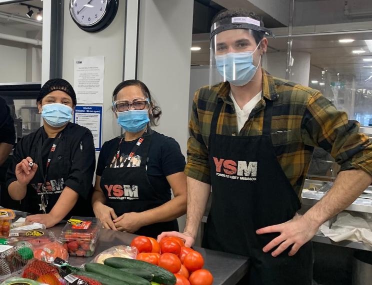 Three volunteers at The Yonge Street Mission (YSM) sort food.