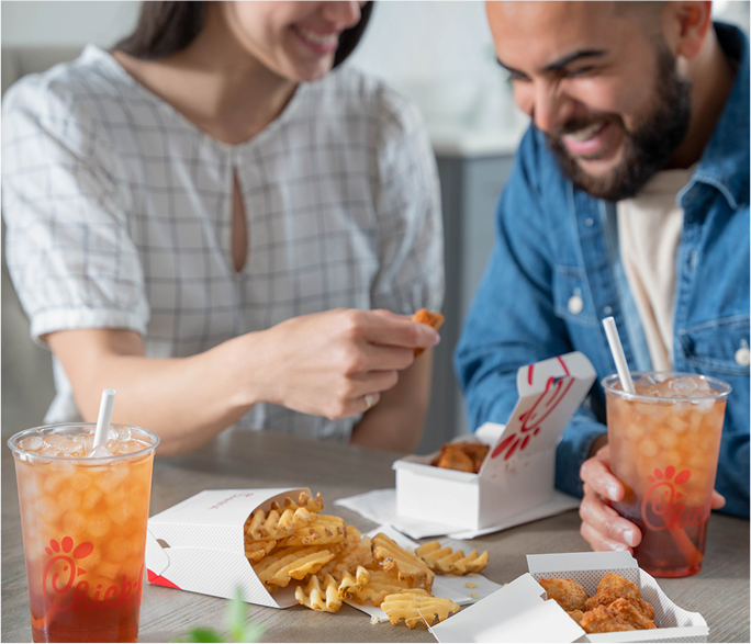 Two people sitting together in red adirondack chairs eating Chick-fil-A food