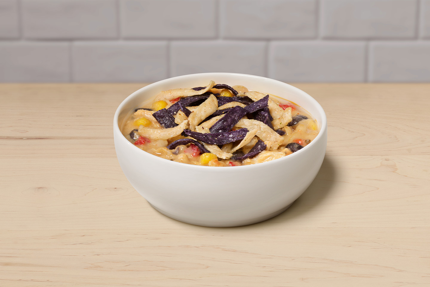 A bowl of Chicken Tortilla Soup on a wooden table with a gray tiled background