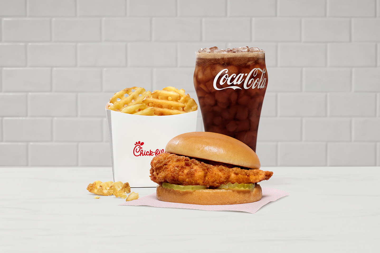 Chick-fil-A® Chicken Sandwich with Waffle Fries and a Coca-Cola® on a white tiled background