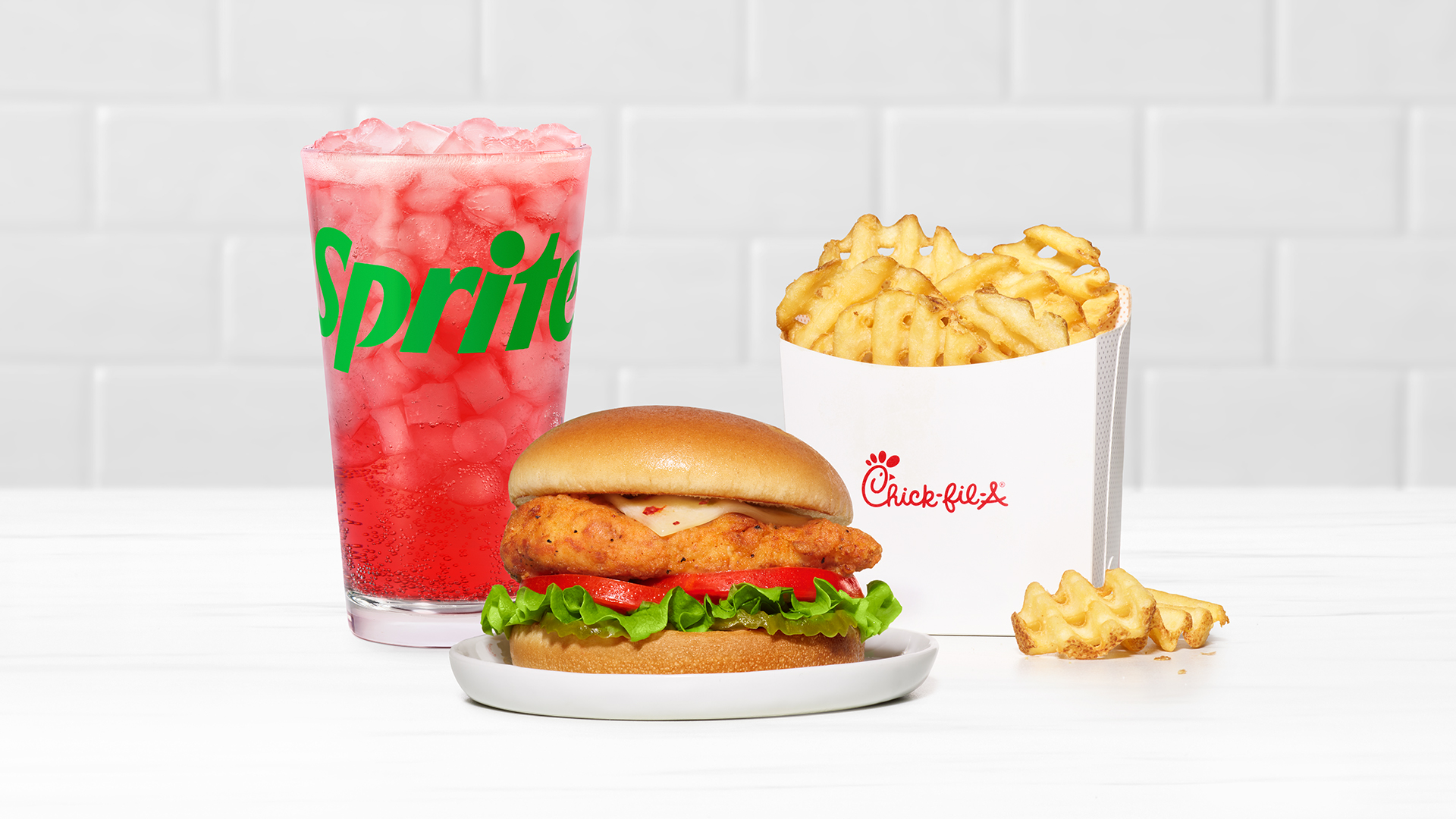 Spicy Deluxe Sandwich on a white plate with Waffle Fries and a Strawberry Hibiscus & Sprite® on a white tiled background