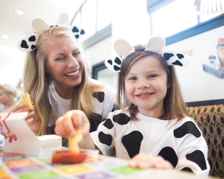 Two Chick-fil-A Guests sitting at a table eating waffle fries in cow-themed attire.
